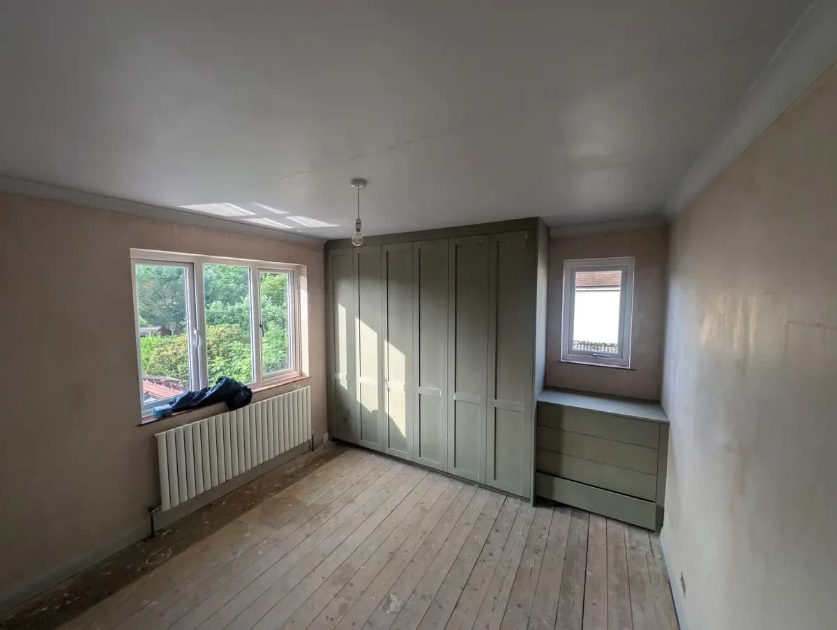 The same bedroom before work: bare plaster walls, stripped floorboards and the fitted wardrobes still in pale primer